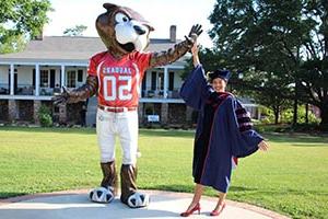 Business student in cap and gown high fiving Southpaw statue on campus.